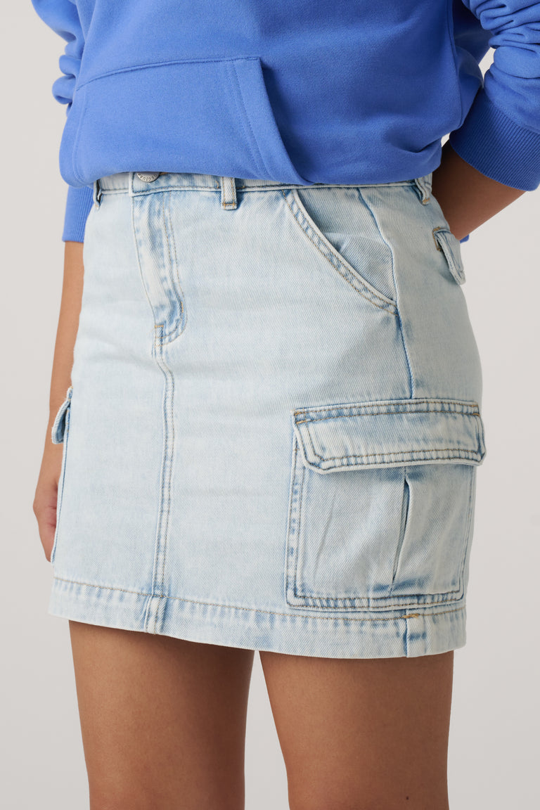 Woman wearing a light wash denim cargo skirt with utility pockets and a blue sweatshirt