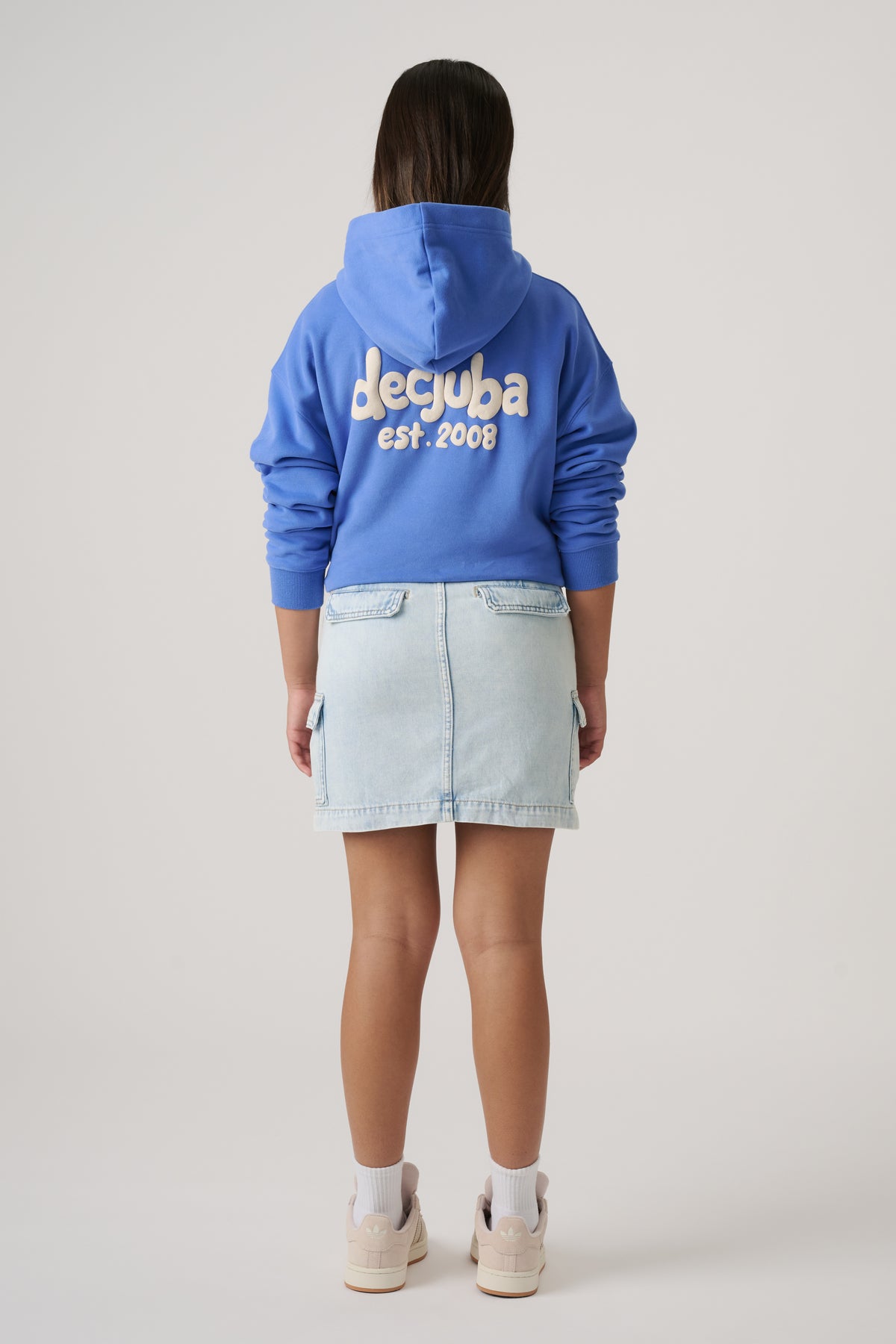 Back view of girl wearing a light denim cargo skirt, blue logo hoodie and sneakers