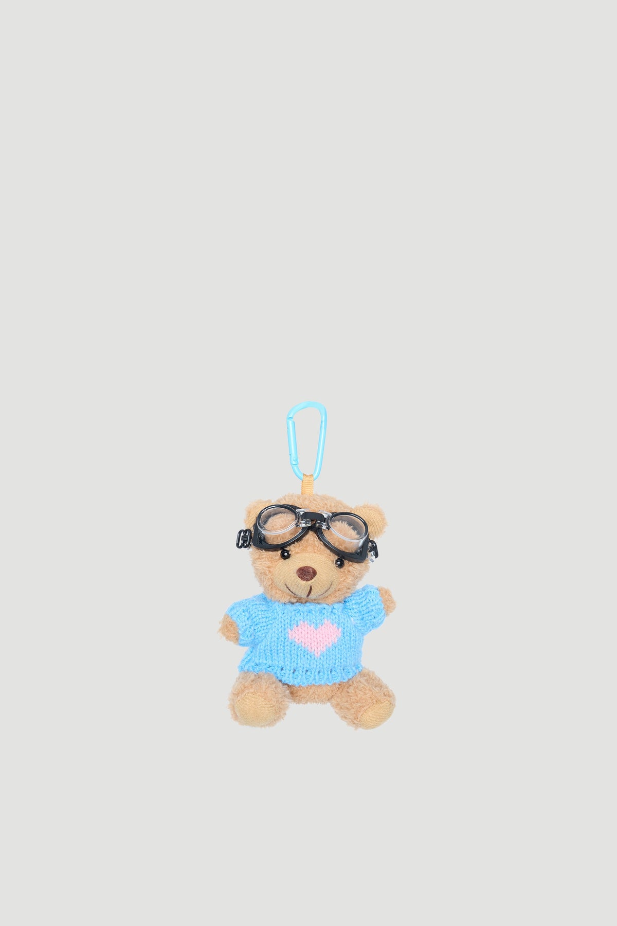 Small plush bear wearing a blue jumper with a pink heart and black aviator goggles, attached to a clip.
