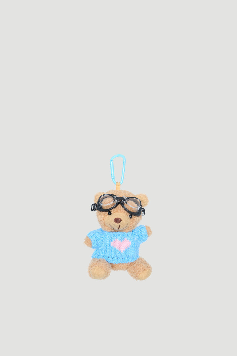Small plush bear wearing a blue jumper with a pink heart and black aviator goggles, attached to a clip.