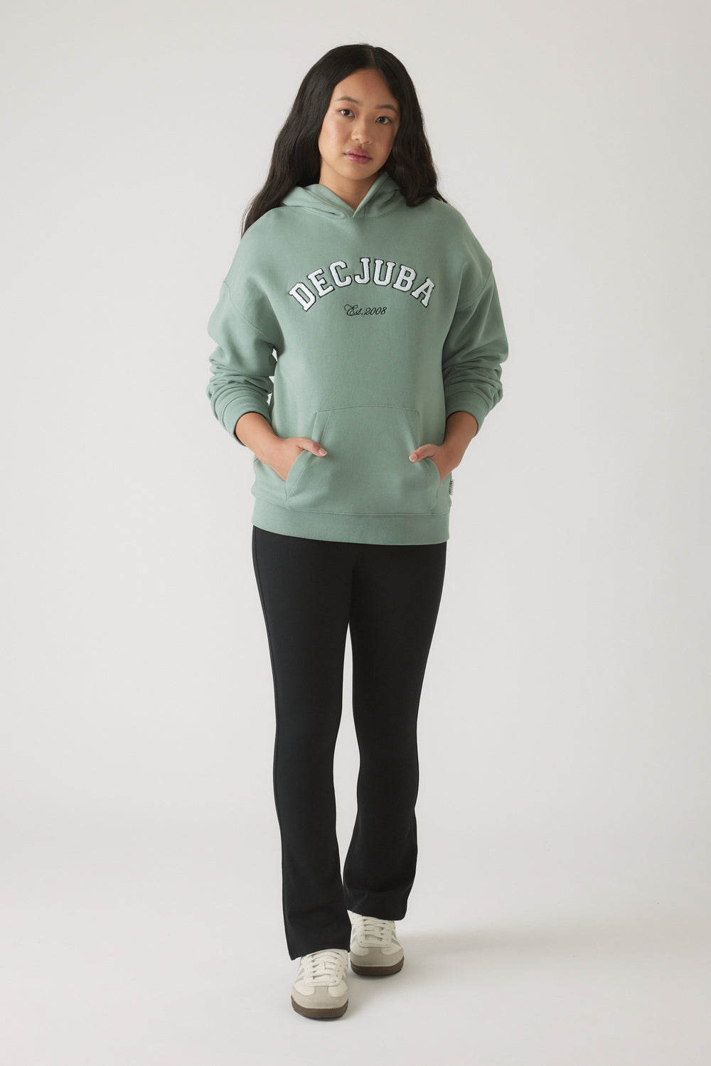 Teen girl wearing an oversized moss green hoodie with pockets, paired with fitted black pants and white sneakers