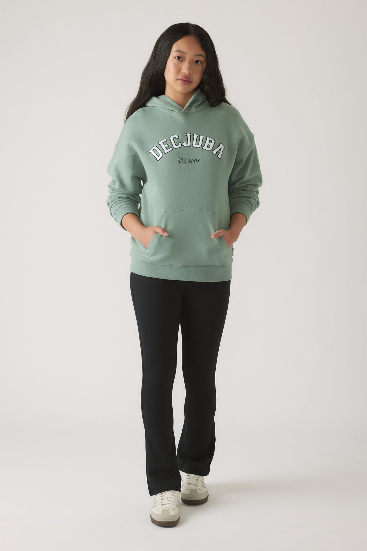 Teen girl wearing an oversized moss green hoodie with pockets, paired with fitted black pants and white sneakers