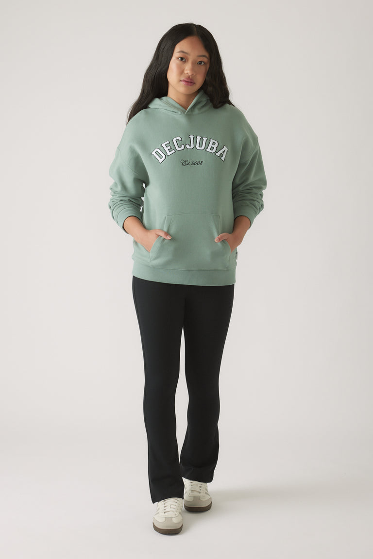 Teen girl wearing an oversized moss green hoodie with pockets, paired with fitted black pants and white sneakers