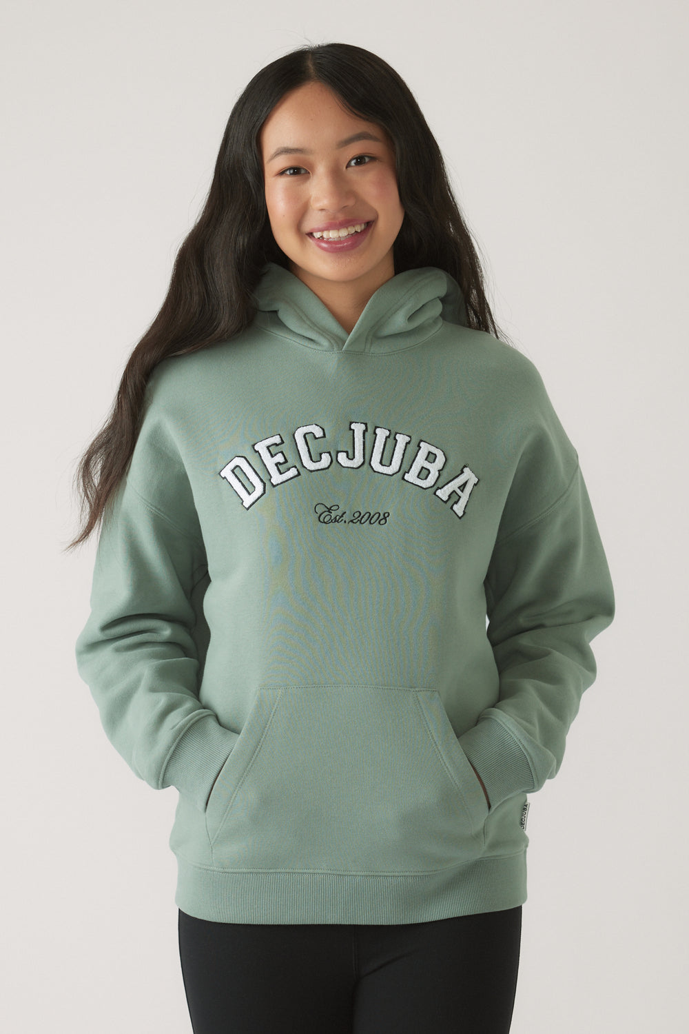 Teen girl smiling in a relaxed pose wearing a soft moss green oversized hoodie with kangaroo pocket and hood