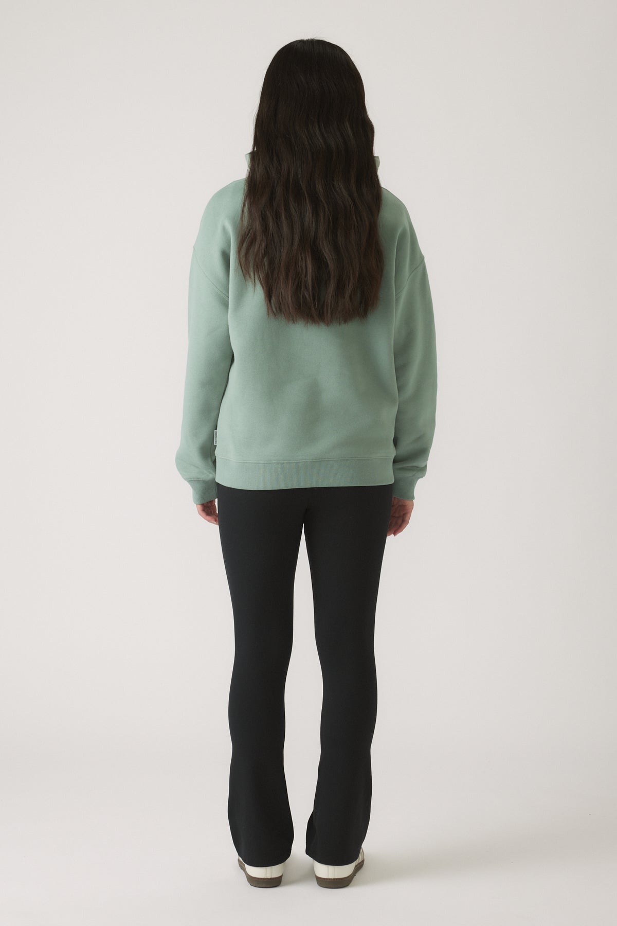 Girl seen from behind wearing a relaxed moss green oversized hoodie paired with fitted black pants and white shoes