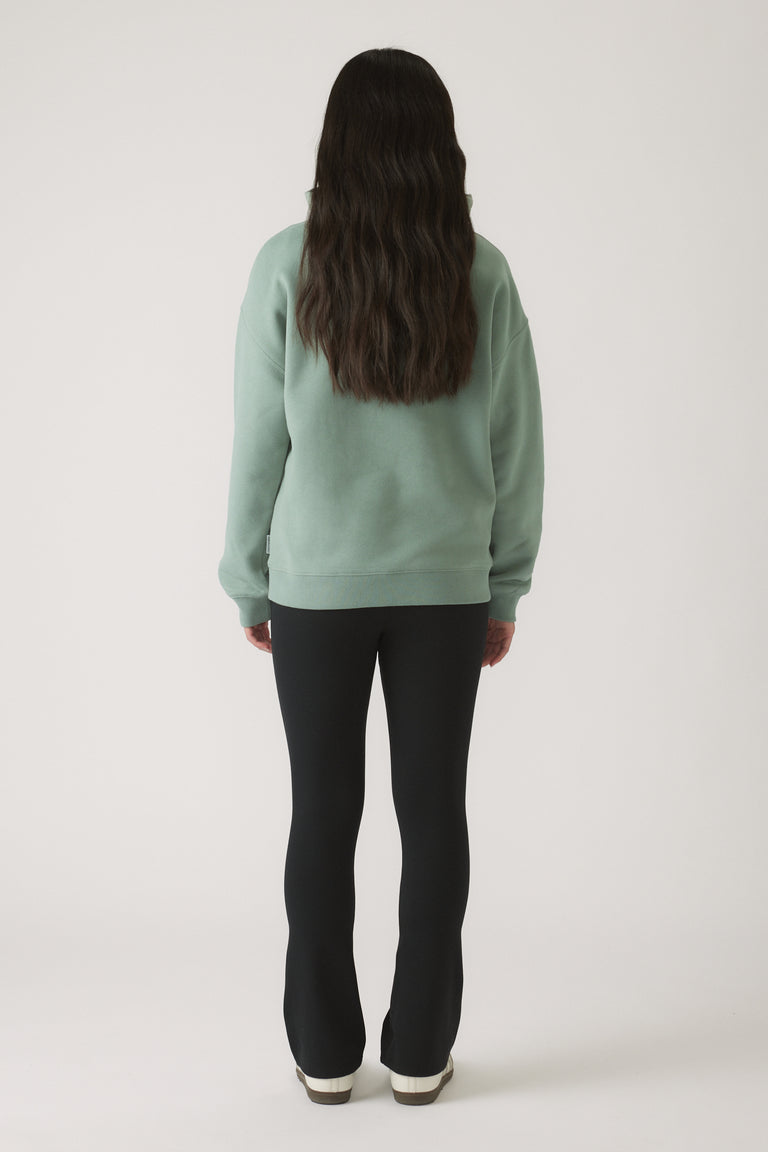Girl seen from behind wearing a relaxed moss green oversized hoodie paired with fitted black pants and white shoes