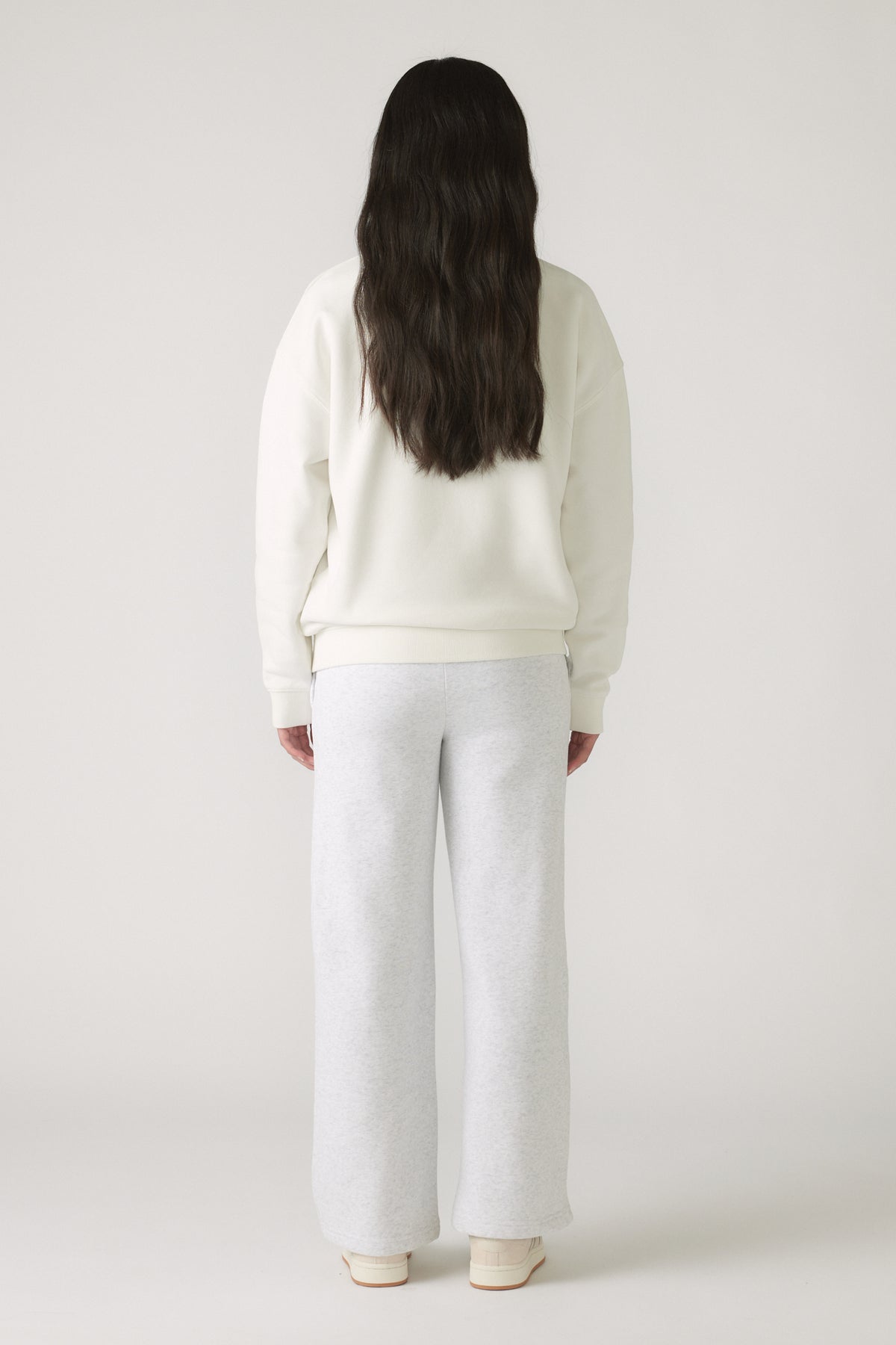 Girl wearing an oversized cream sweatshirt paired with light grey wide-leg pants and white sneakers, seen from behind