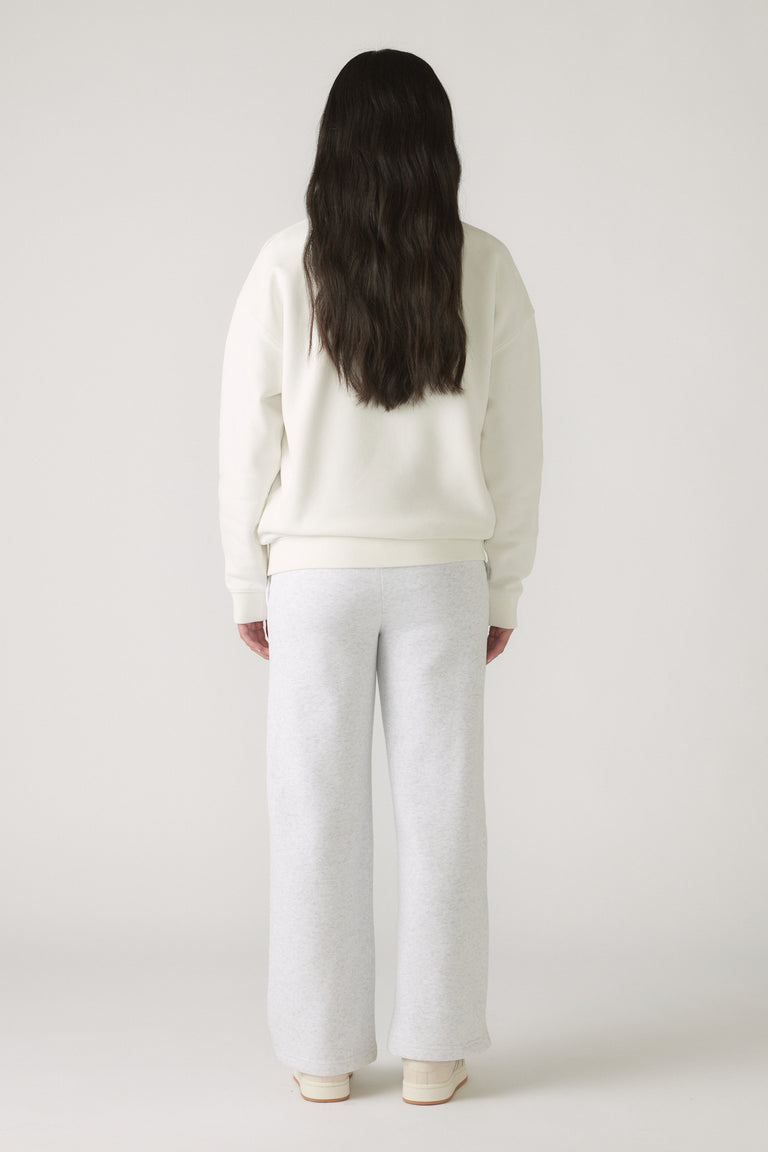Girl wearing an oversized cream sweatshirt paired with light grey wide-leg pants and white sneakers, seen from behind