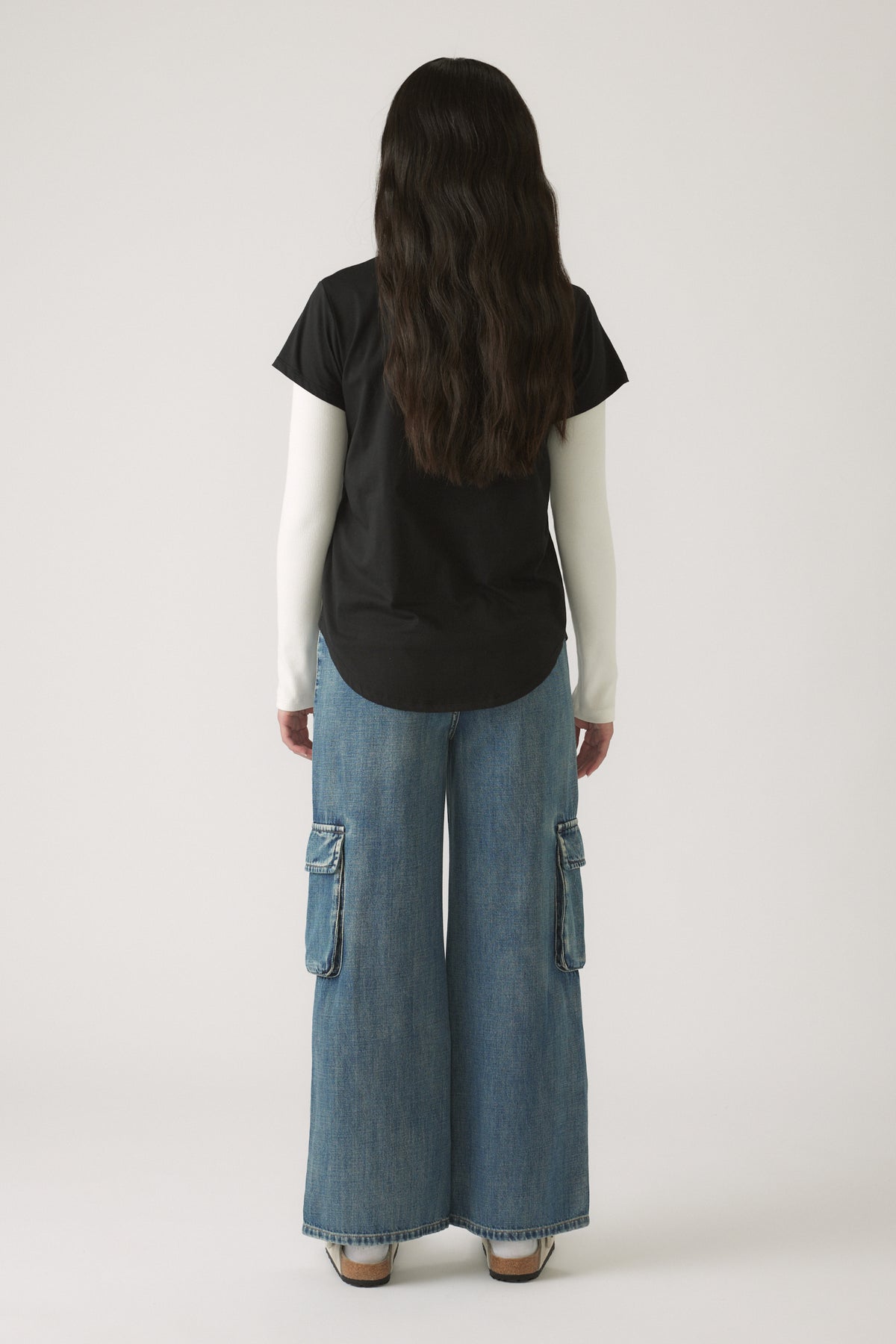 Girl wearing a Girls Decjuba Heritage Tee layered over a long sleeve white top, paired with wide-leg denim cargo pants