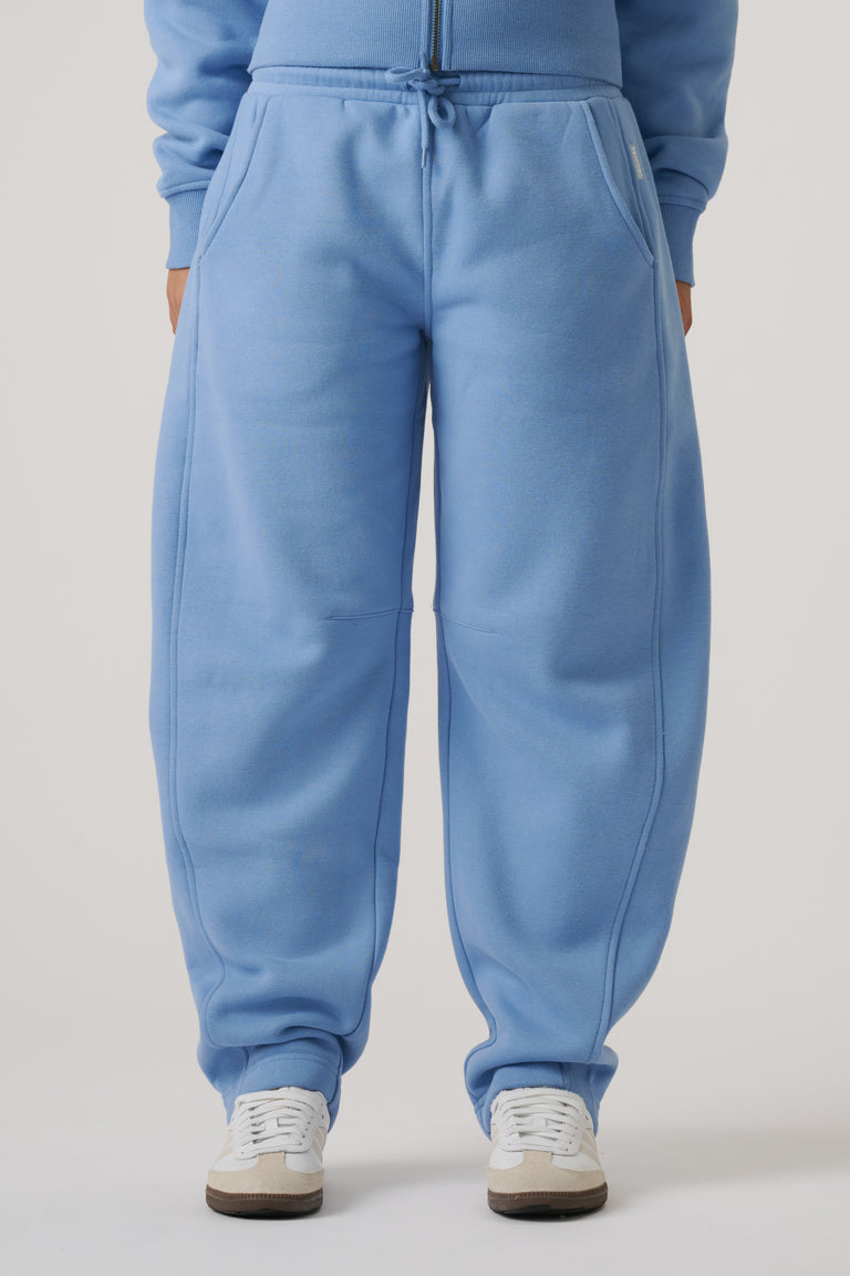 Close-up of relaxed-fit dusty blue barrel leg trackpants with drawstring waist and pockets, styled with sneakers.