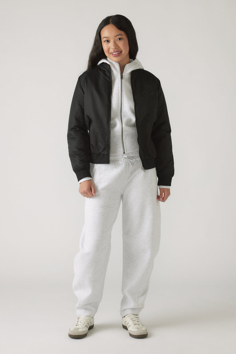 Girl wearing light grey barrel leg pants with a grey zip-up hoodie and a black bomber jacket, smiling confidently