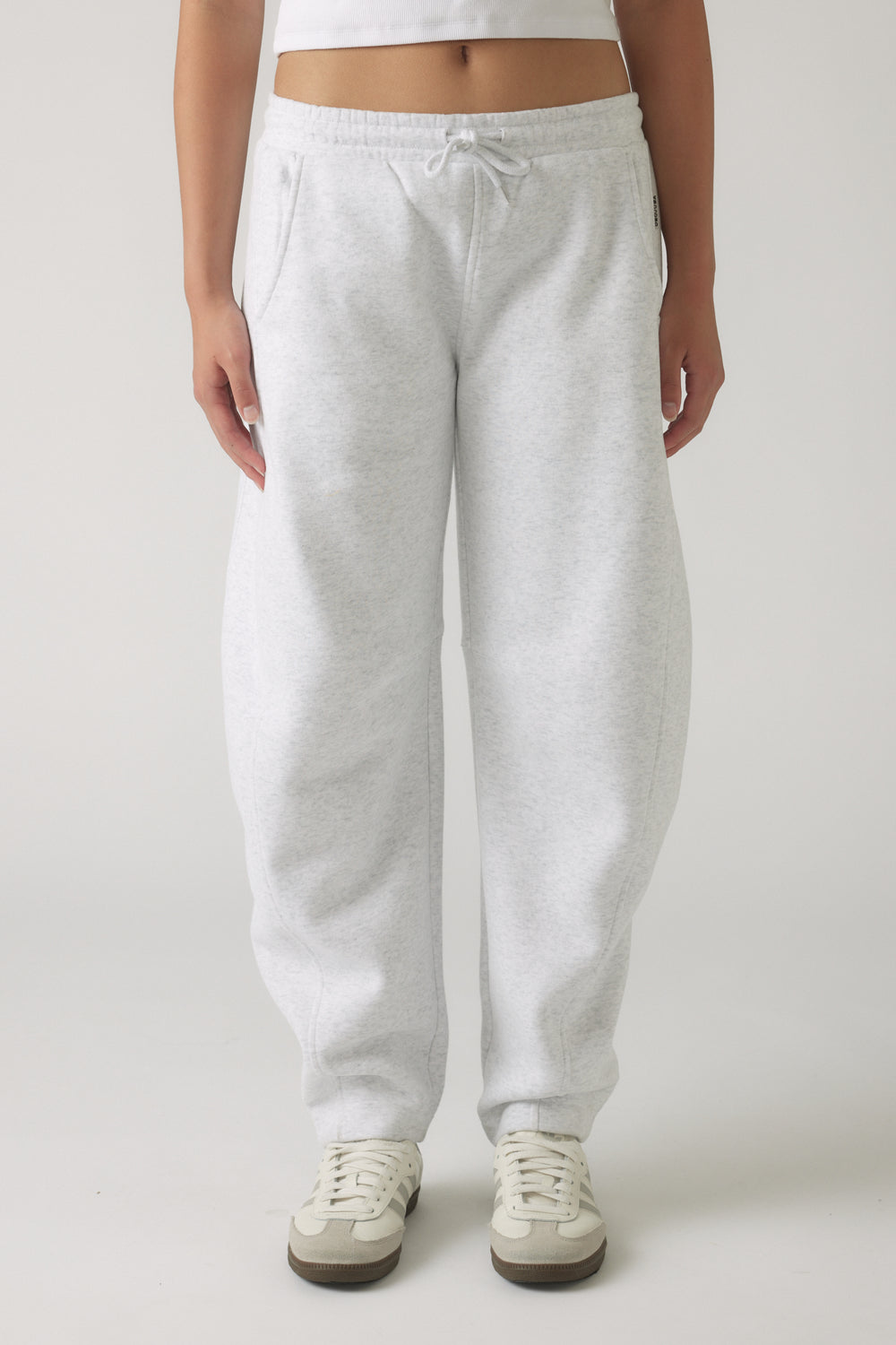 Girl wearing light grey relaxed fit track pants with drawstring waist and white sneakers on a neutral background