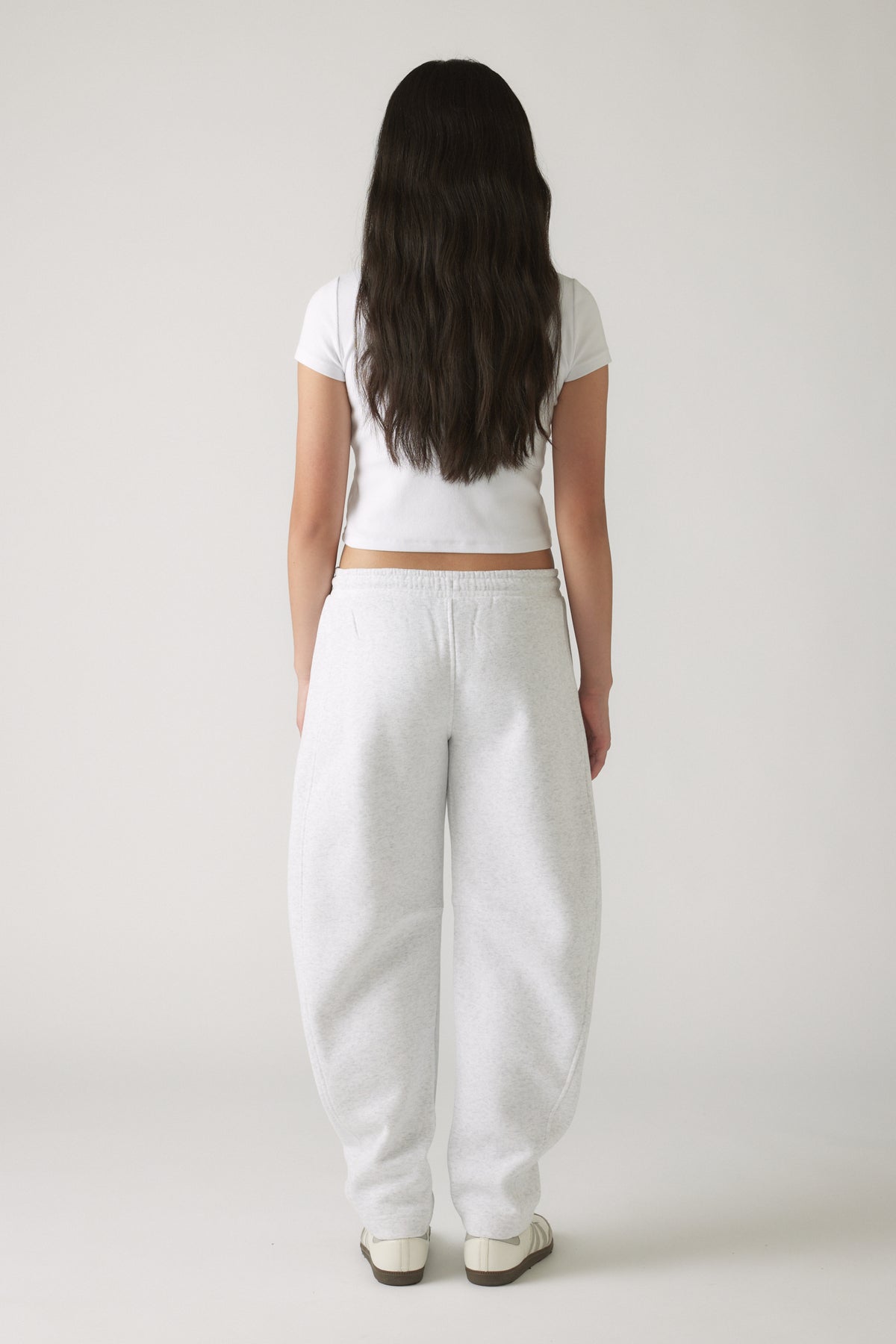 Girl seen from behind wearing relaxed light grey barrel leg track pants paired with a cropped white tee and sneakers