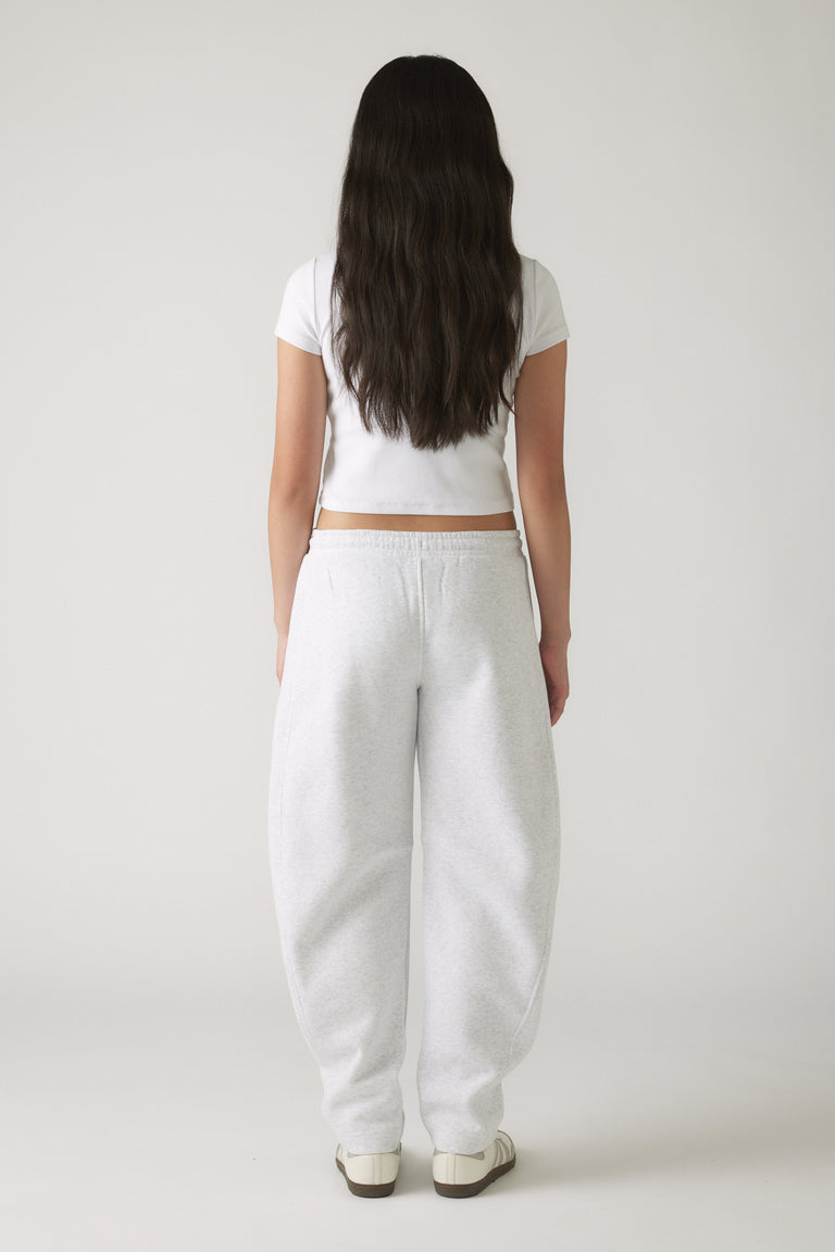 Girl seen from behind wearing relaxed light grey barrel leg track pants paired with a cropped white tee and sneakers