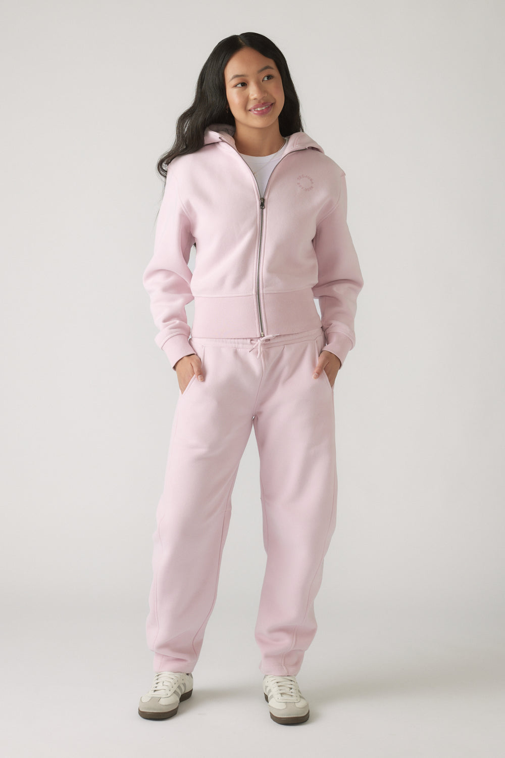 Girl wearing soft mauve barrel leg track pants paired with a matching zip-up hoodie and white sneakers