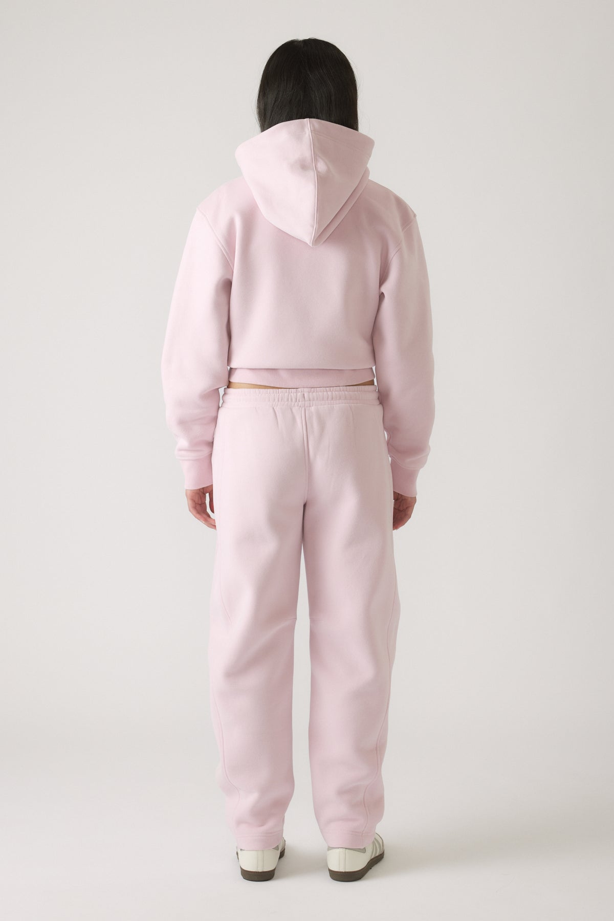 Back view of girl wearing soft mauve barrel leg pants with matching cropped hoodie and casual sneakers.
