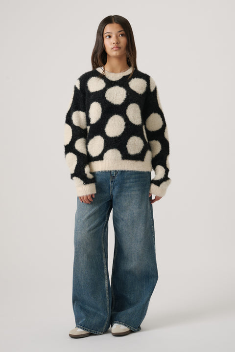 Teen girl wearing a soft black and cream polka dot knit jumper paired with wide-leg blue denim jeans and sneakers