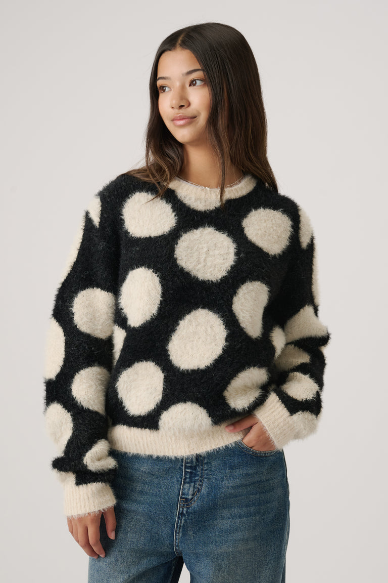 Girl wearing a cozy black crew knit jumper with large cream polka dots paired with relaxed blue jeans