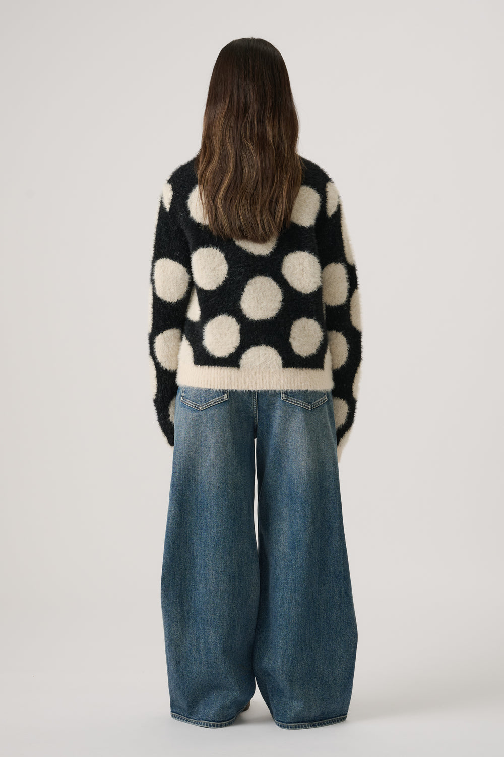 Girl wearing a black and cream fluffy knit jumper with large polka dots paired with wide-leg blue denim jeans