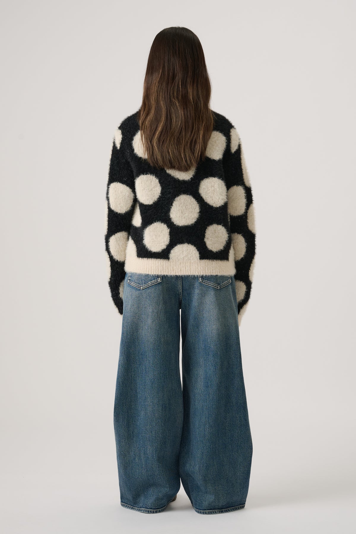Girl wearing a black and cream fluffy knit jumper with large polka dots paired with wide-leg blue denim jeans