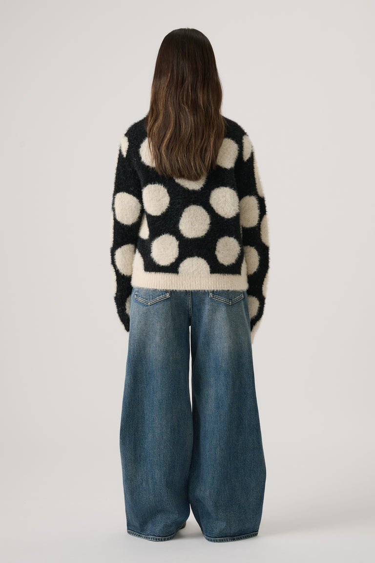 Girl wearing a black and cream fluffy knit jumper with large polka dots paired with wide-leg blue denim jeans