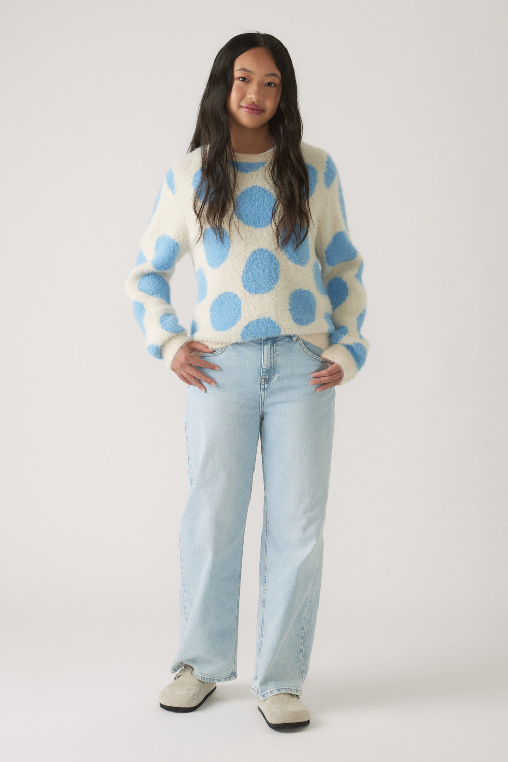 Girl wearing a cozy fluffy knit jumper with blue polka dots paired with light wash wide-leg jeans for casual style.