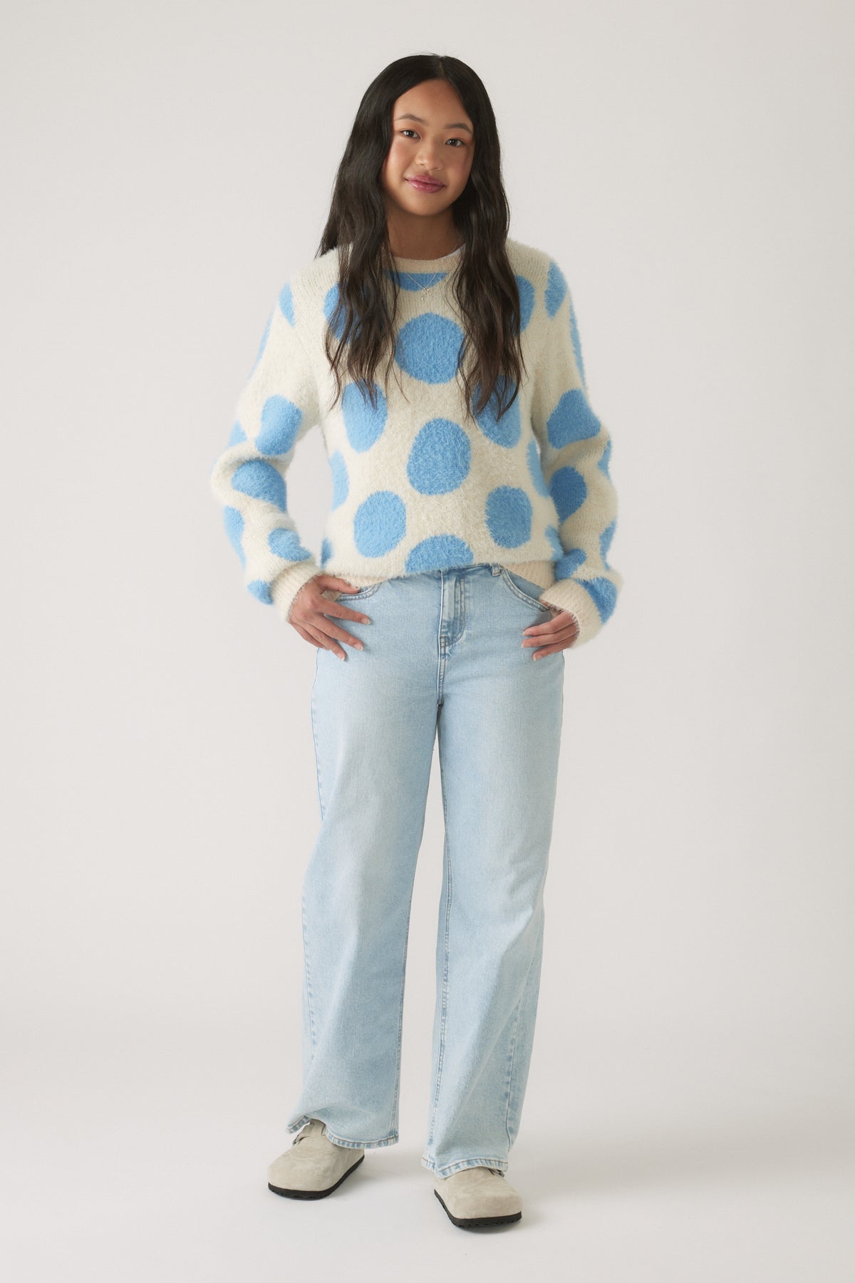 Girl wearing a cozy fluffy knit jumper with blue polka dots paired with light wash wide-leg jeans for casual style.