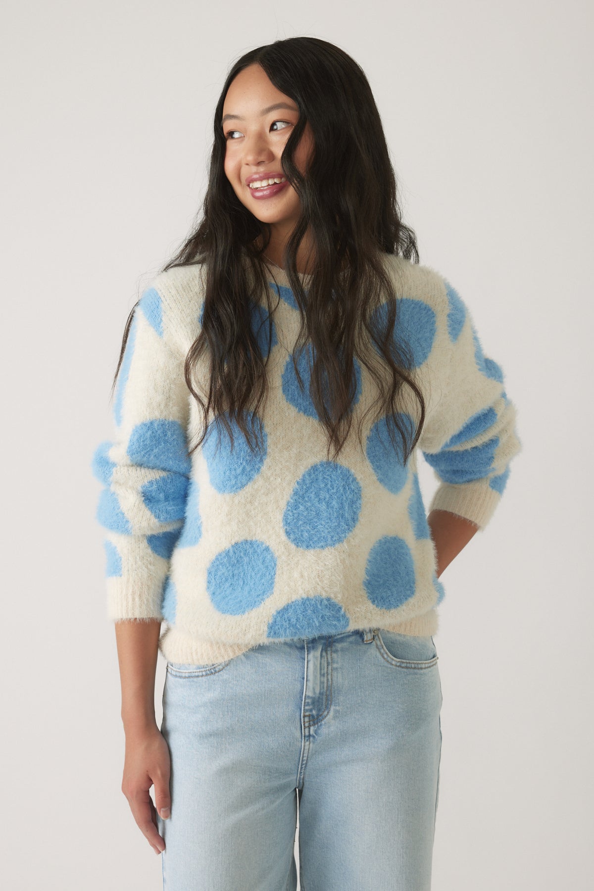 Girl wearing a soft, cream-colored knit jumper with large blue polka dots, paired with light wash casual jeans