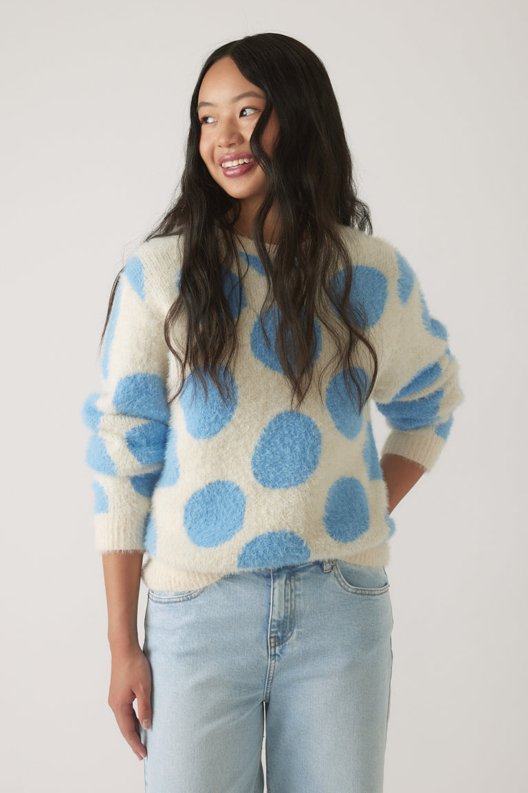 Girl wearing a soft, cream-colored knit jumper with large blue polka dots, paired with light wash casual jeans
