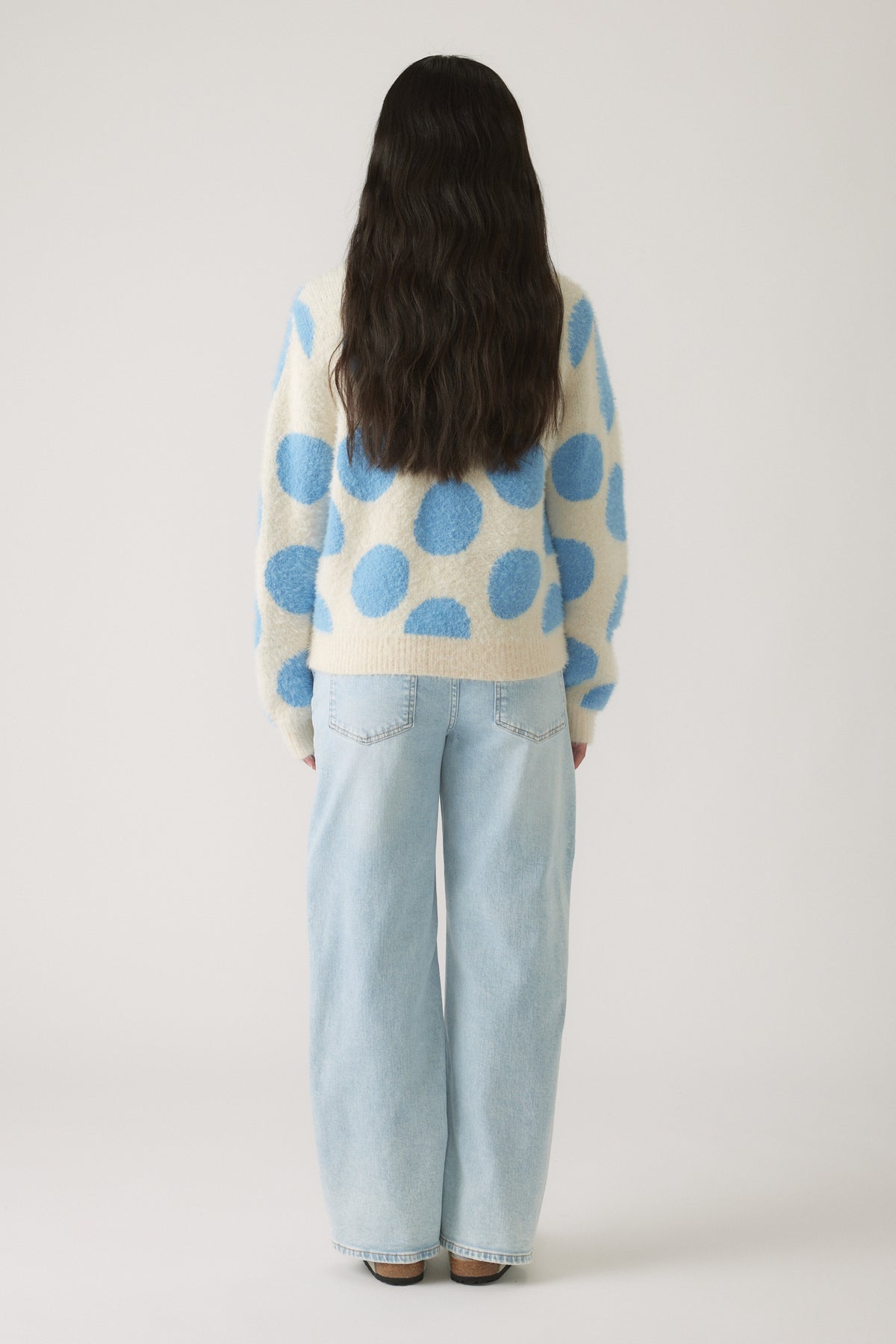 Rear view of girl wearing a cozy cream jumper with large blue polka dots paired with light blue wide-leg jeans