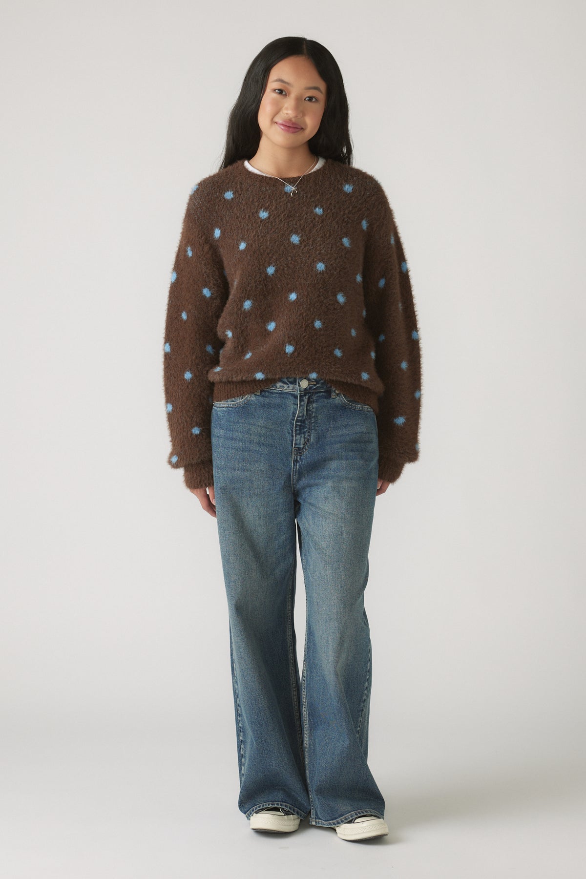 Girl wearing a brown Girls Fluffy Crew Knit Jumper with blue polka dots styled with relaxed blue denim jeans and white sneakers.