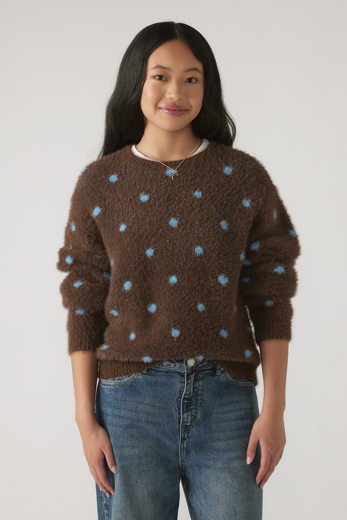 Girl wearing a Girls Fluffy Crew Knit Jumper in brown with soft blue polka dots, styled with casual denim jeans by DECJUBA
