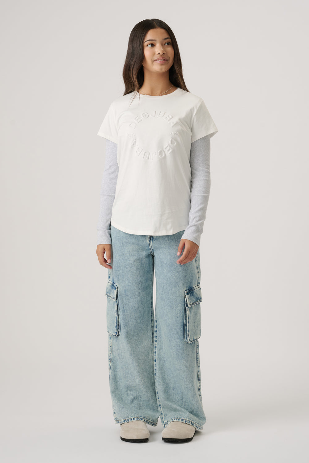 Girl wearing a vanilla embossed tee layered over a long-sleeve top, paired with light wash wide-leg denim cargo pants.