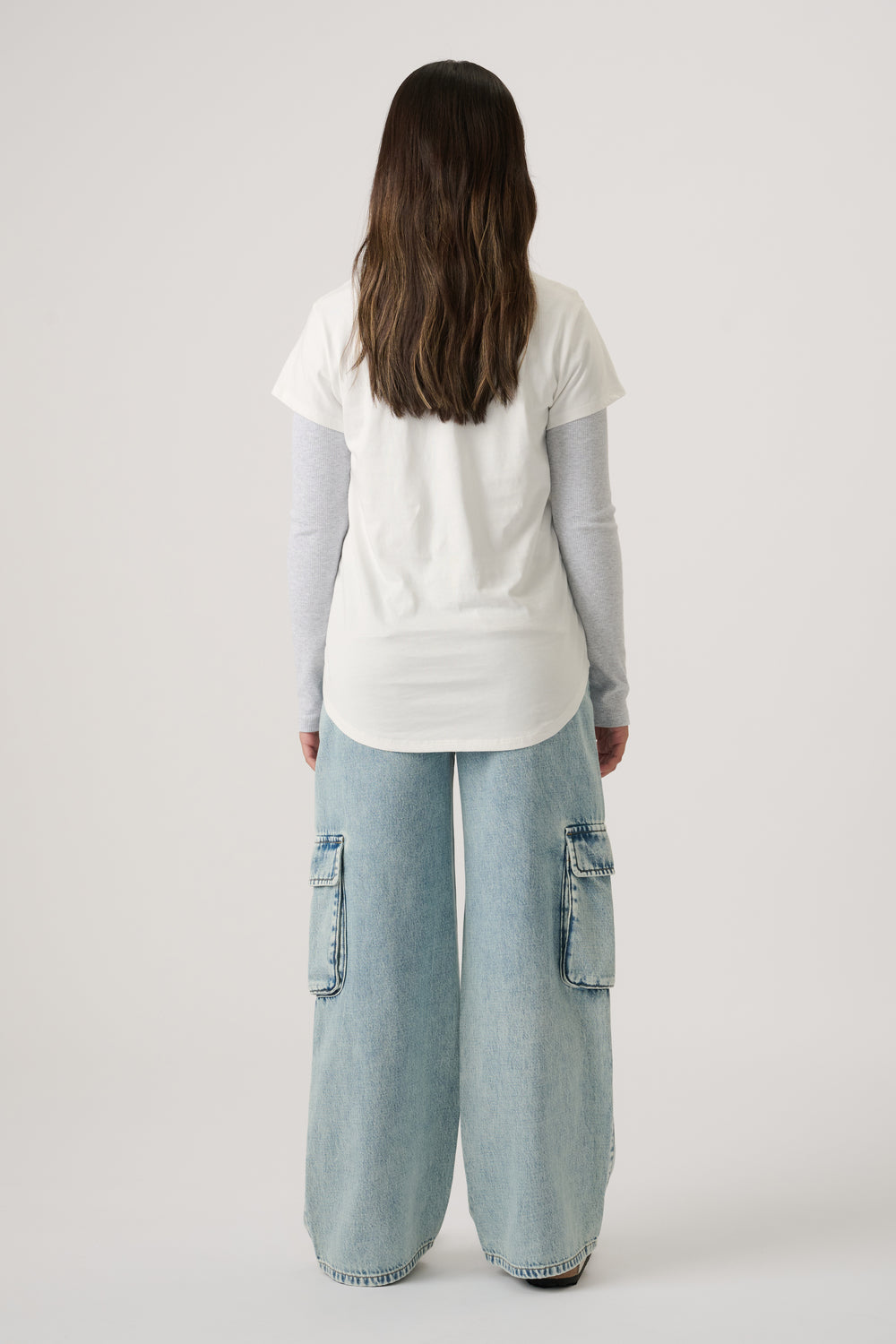 Girl wearing a white tee layered over a long-sleeve top, paired with light wash wide-leg denim cargo jeans.