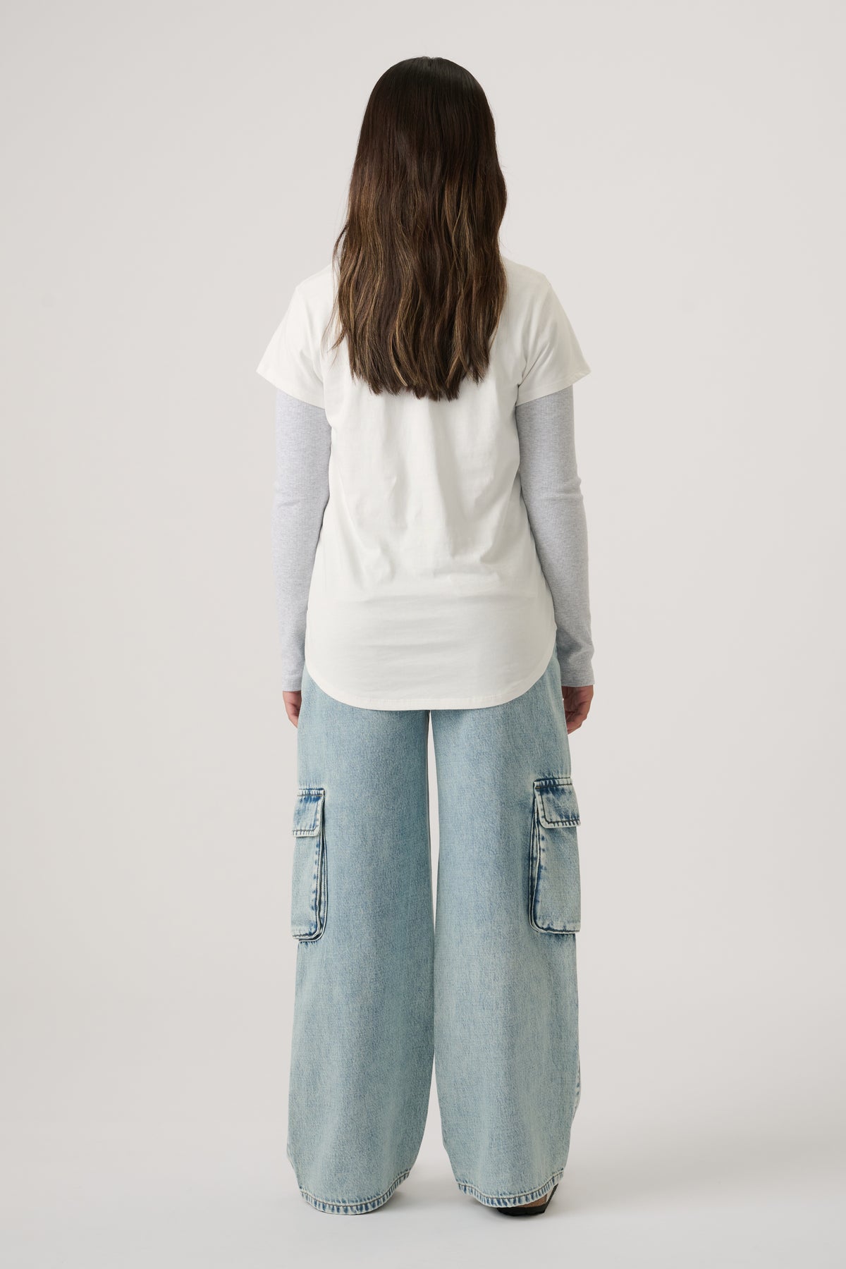 Girl wearing a white tee layered over a long-sleeve top, paired with light wash wide-leg denim cargo jeans.