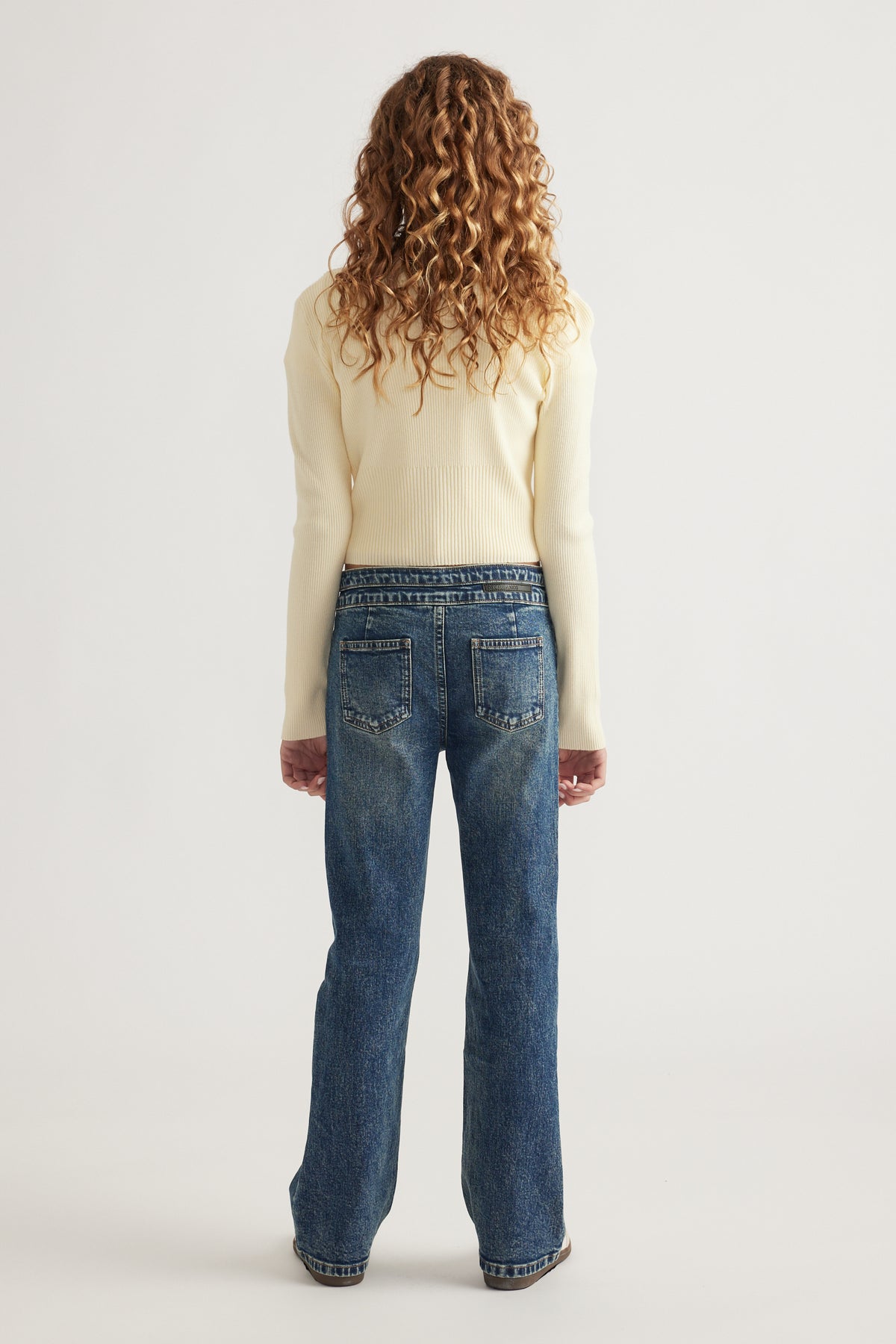 Rear view of girl wearing medium wash straight leg jeans paired with a fitted cream knit sweater