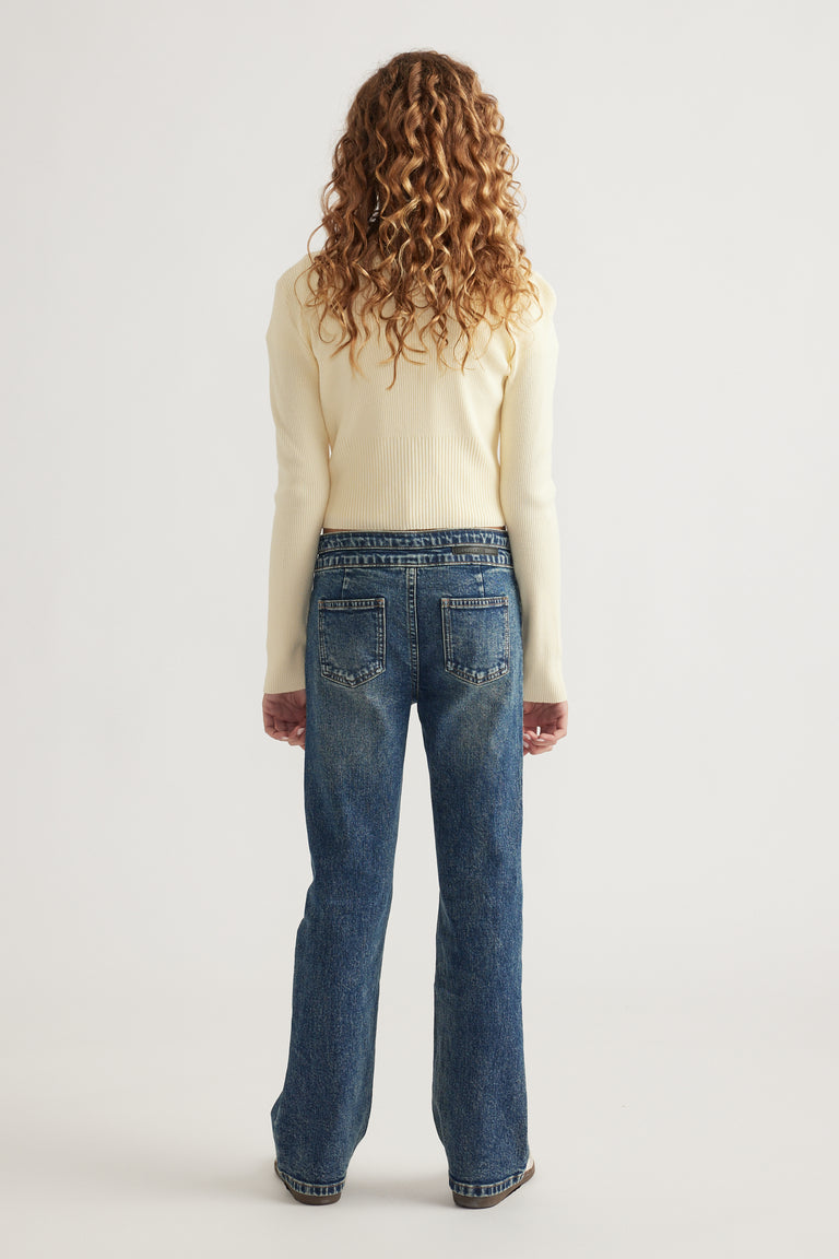 Rear view of girl wearing medium wash straight leg jeans paired with a fitted cream knit sweater