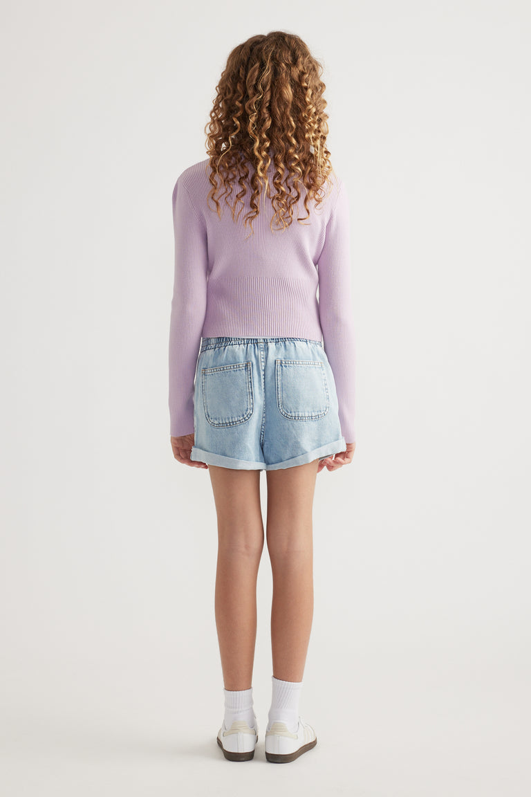 Back view of girl wearing a lilac knit sweater with denim shorts, socks and sneakers