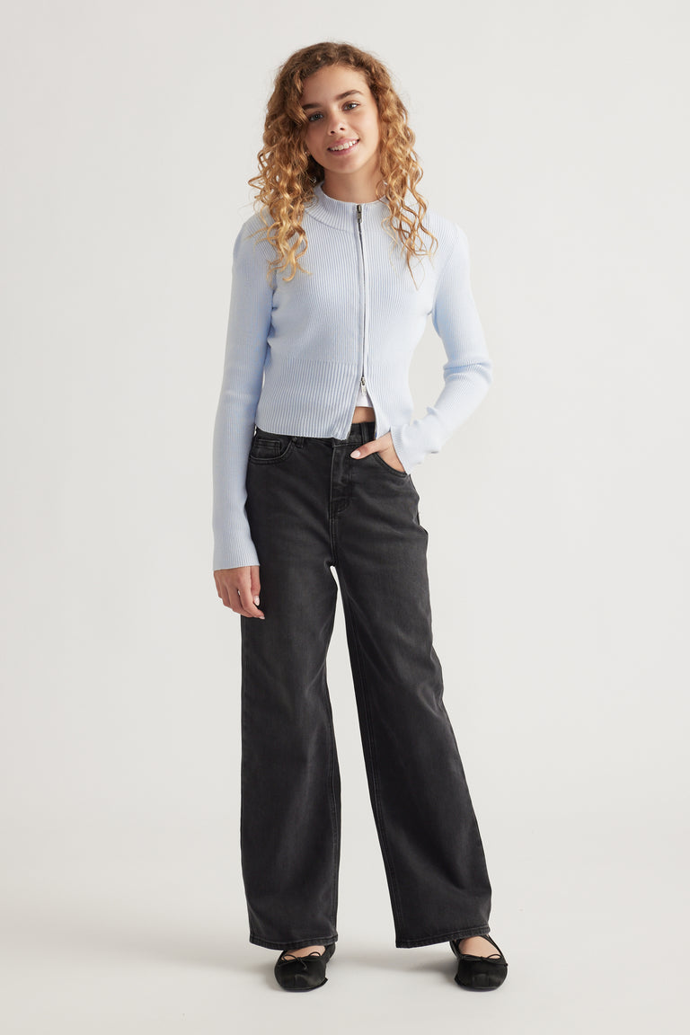 Teen girl smiling wearing a light blue zip-up knit with a stand collar and relaxed black wide-leg jeans