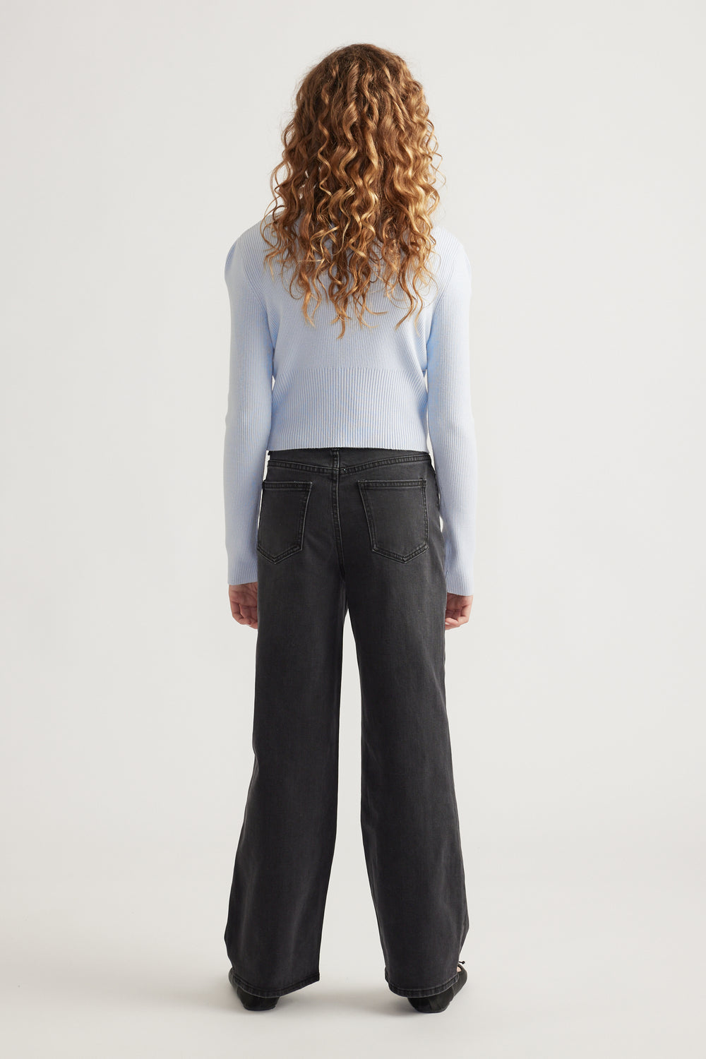 Rear view of girl with curly hair wearing a pale blue fitted knit top paired with loose black wide-leg jeans