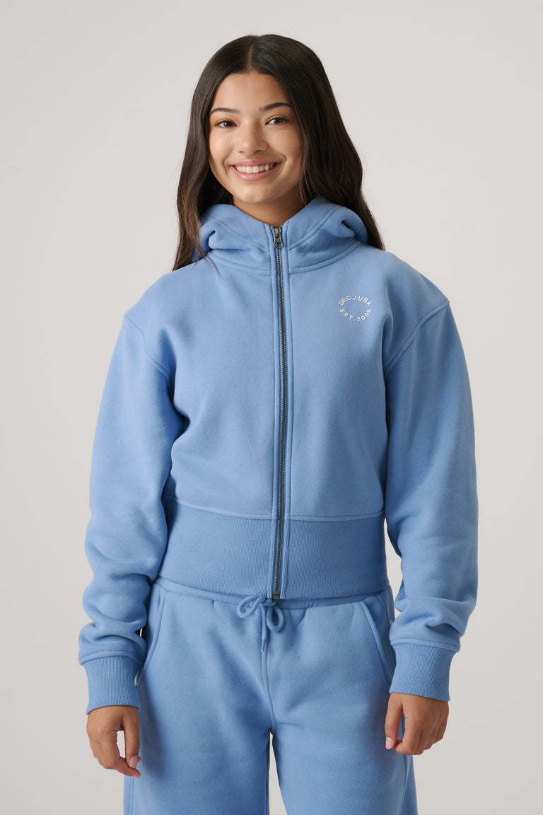 Teen girl wearing a dusty blue cropped zip-up hoodie with a hood, paired with matching relaxed sweatpants.