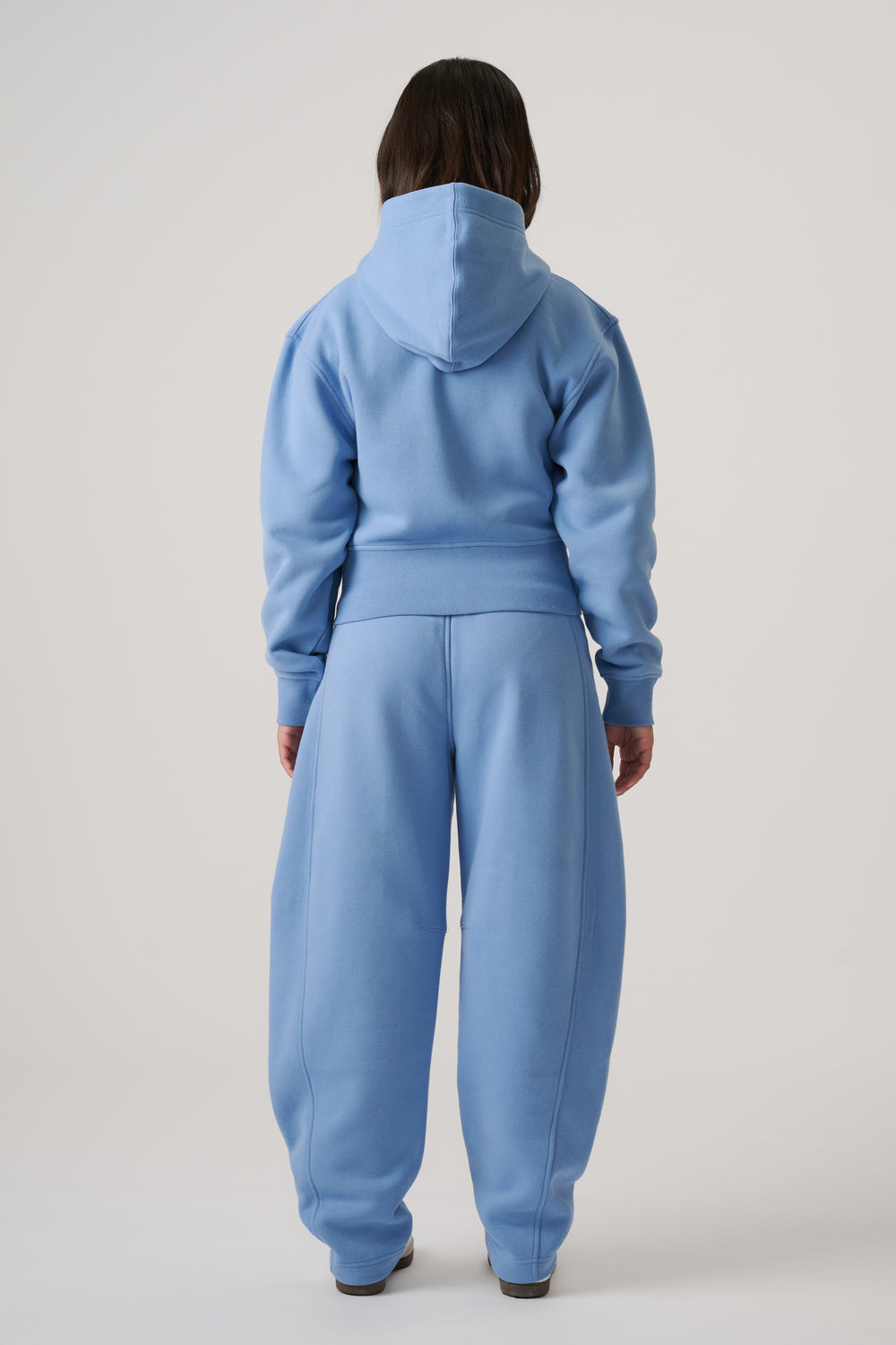 Girl wearing a relaxed dusty blue cropped hoodie with matching wide-leg sweatpants, standing with back facing camera.