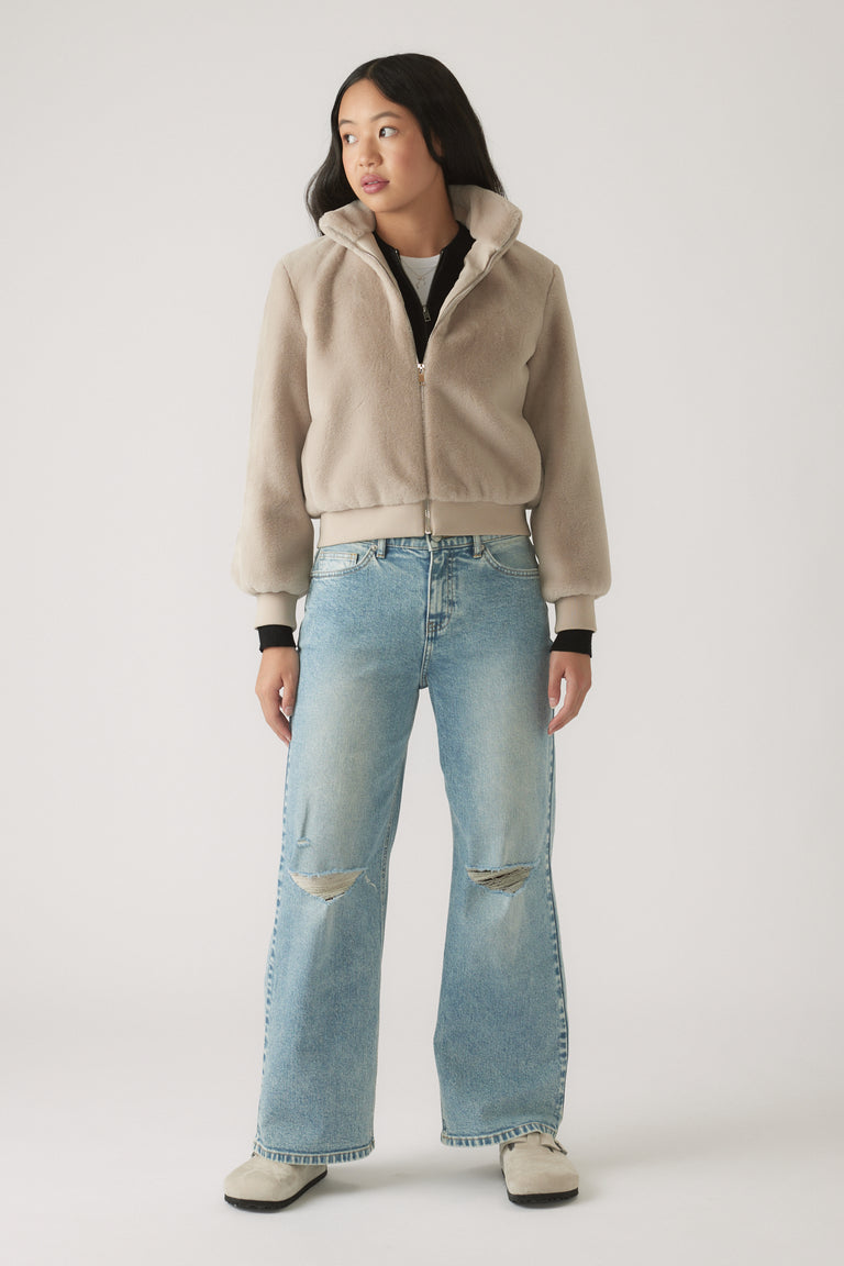 Teen girl wearing light blue baggy ripped jeans paired with a beige zip-up fleece jacket and casual shoes