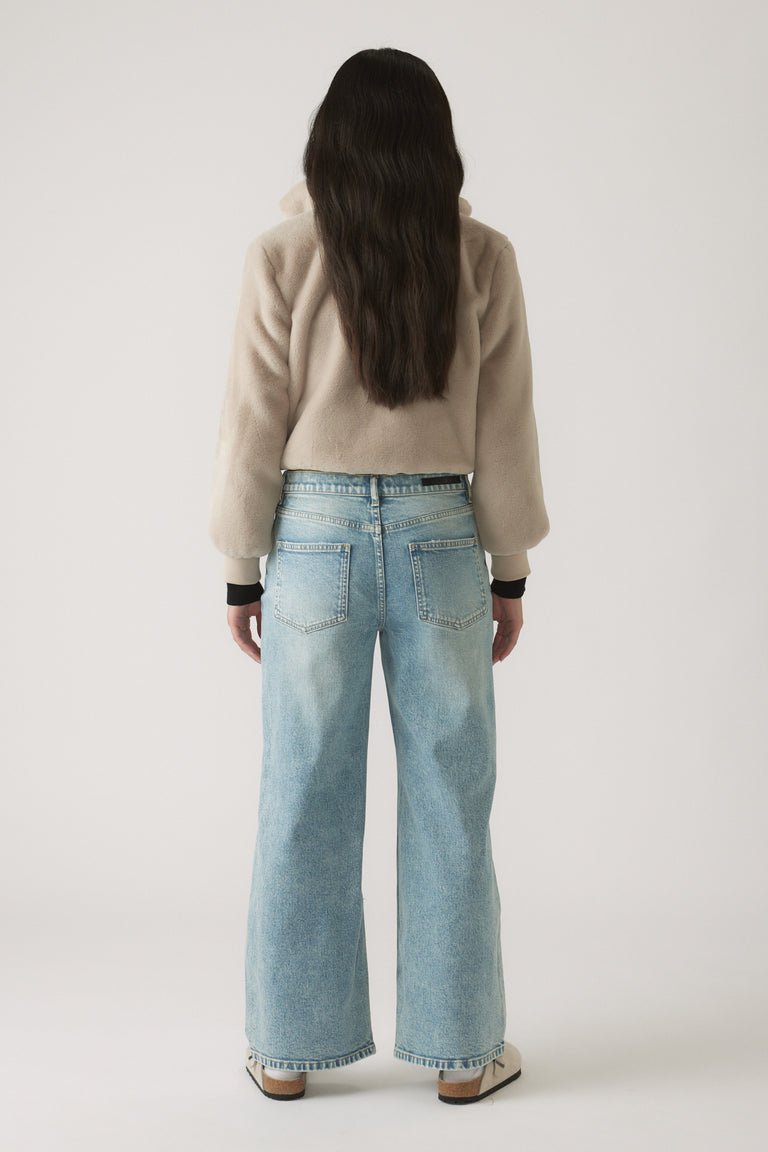 Back view of a girl wearing light blue baggy distressed jeans paired with a soft beige long-sleeve top.