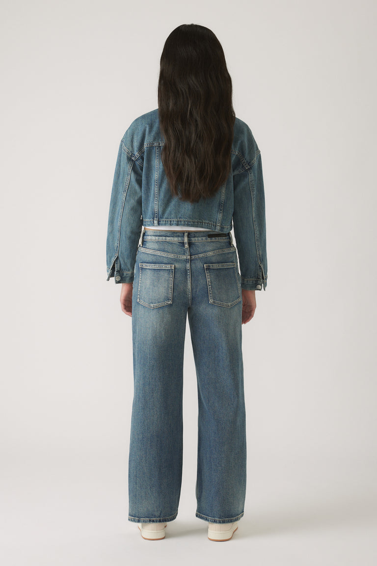Girl wearing blue Girls Gigi Baggy Ripped Jean styled with a cropped denim jacket and white sneakers, shown from behind