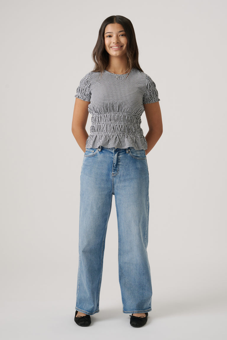 Girl wearing a fitted black-and-white gingham top with ruffled waist paired with relaxed light blue denim jeans and black flats