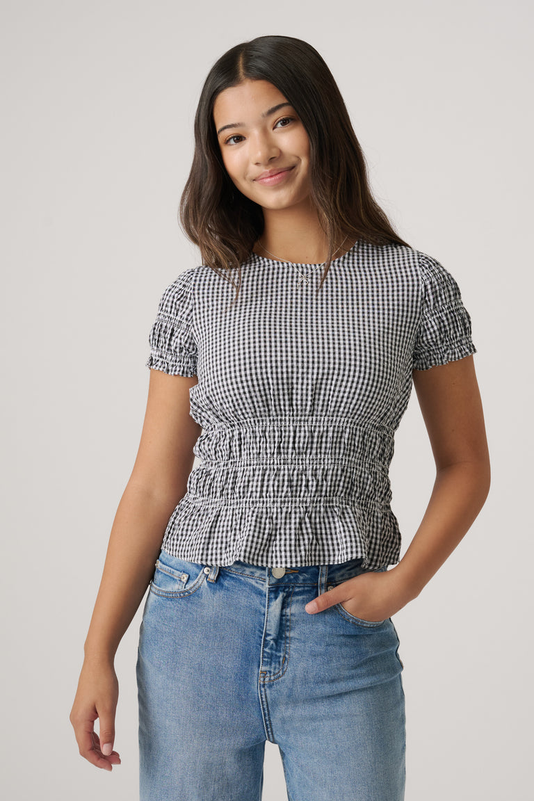 Girl wearing a black and white gingham top with ruched waist and sleeves paired with light blue denim jeans