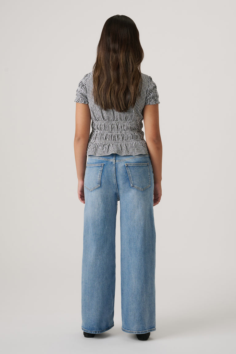 Back view of girl wearing a fitted black-and-white gingham top paired with relaxed wide-leg blue jeans