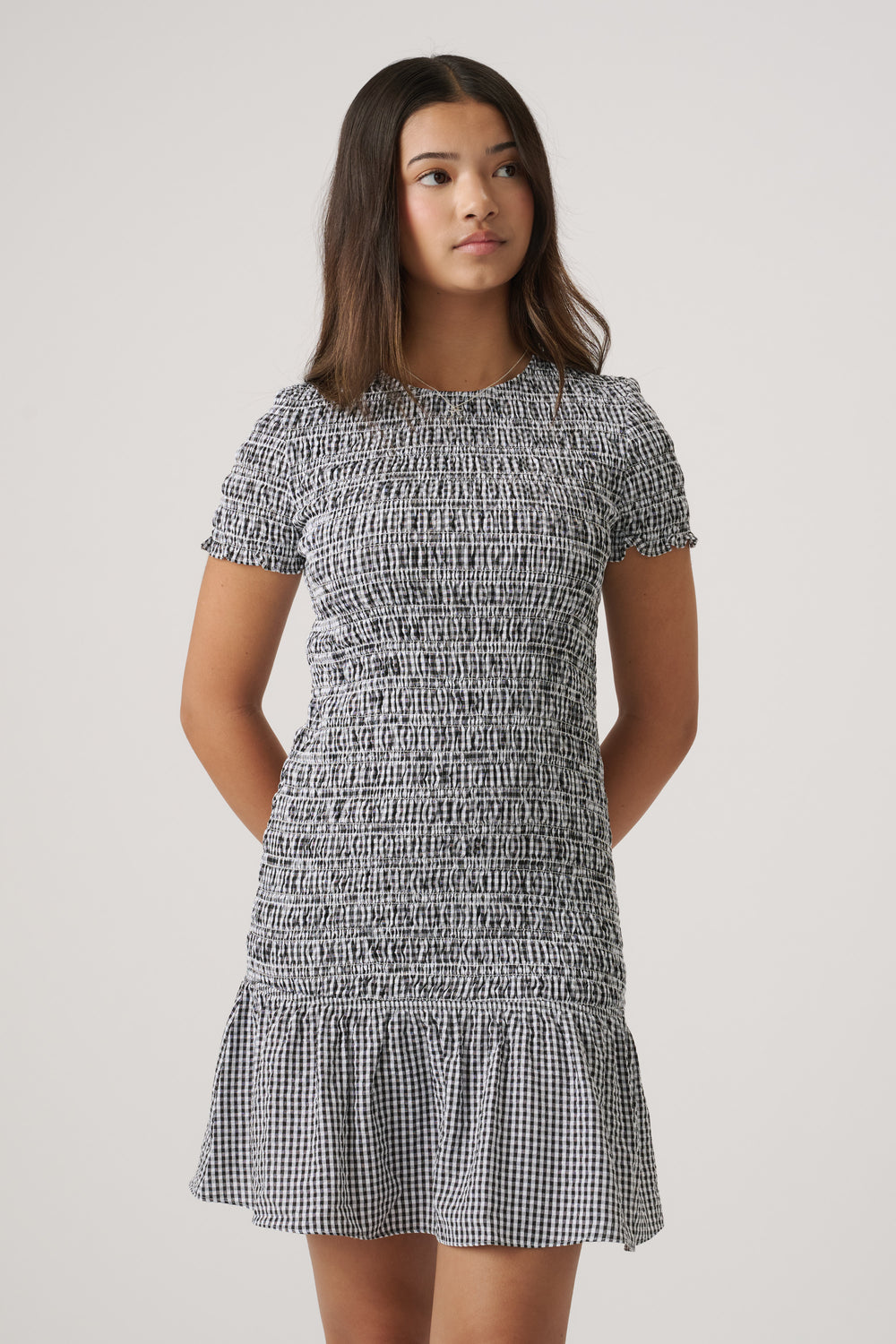 Girl wearing a fitted black and white gingham dress with short sleeves and a flared ruffle hem detail.