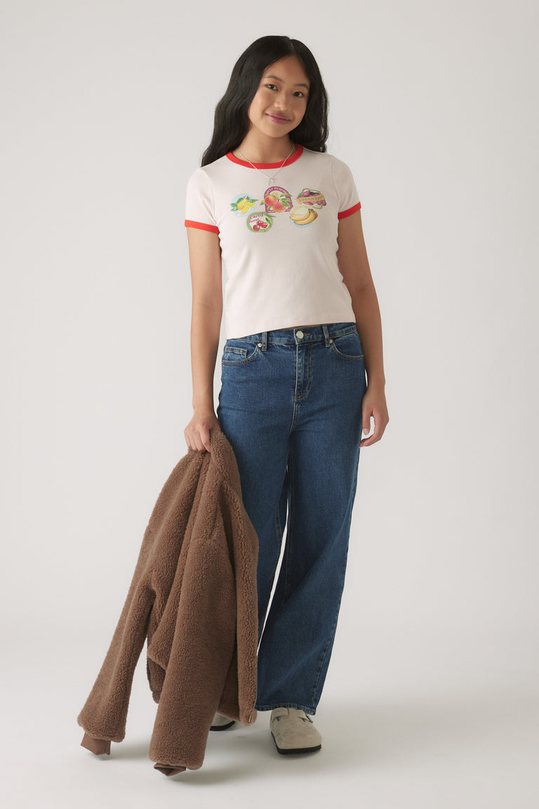 Girl wearing a cropped ringer tee with vibrant patches, paired with wide-leg blue denim jeans and holding a brown teddy jacket